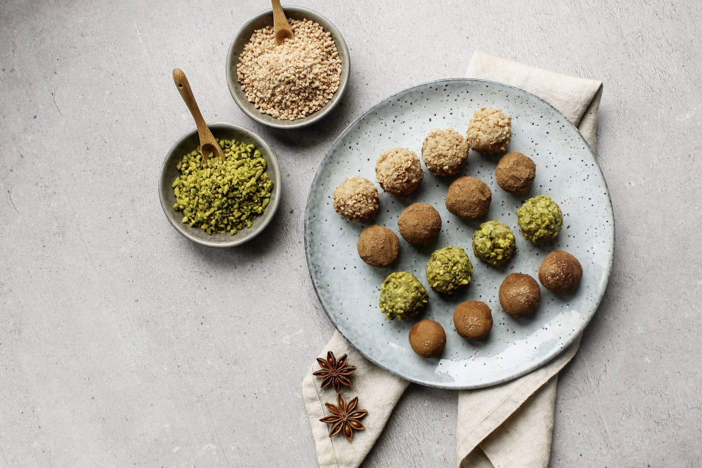 Marzipan balls with bourbon vanilla sugar on a light blue plate with 2 bowls full of pistachios and hazelnut brittle