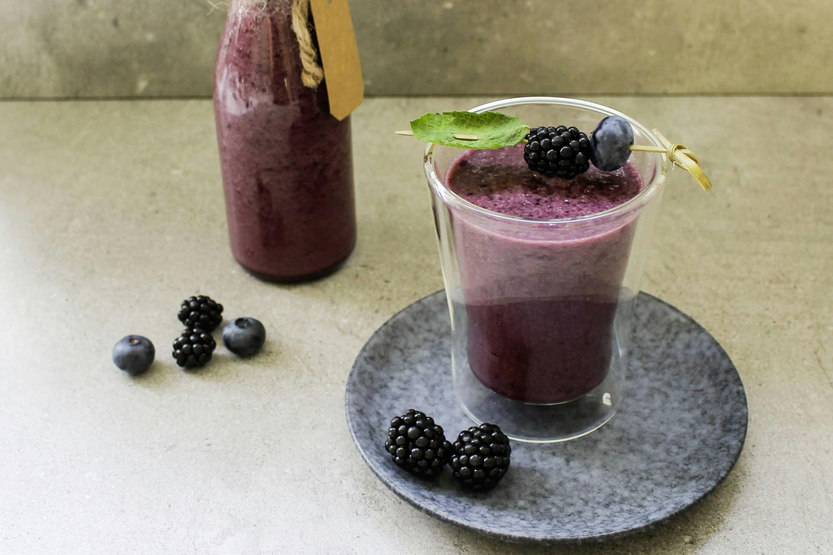 Blackberry and banana shake in a glass and a bottle garnished with fresh berries
