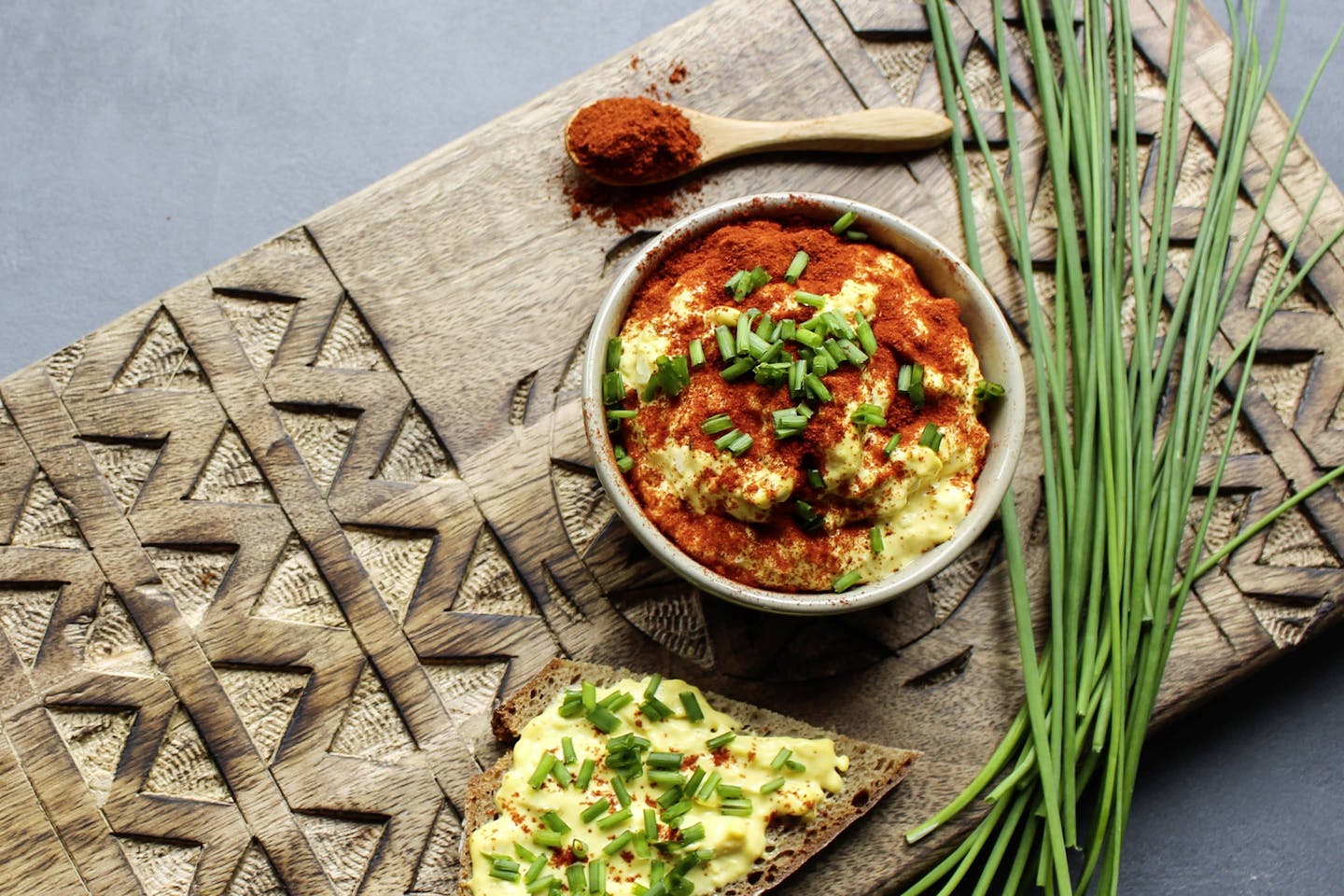 Egg spread with smoked paprika on a wooden board with a bunch of fresh chives