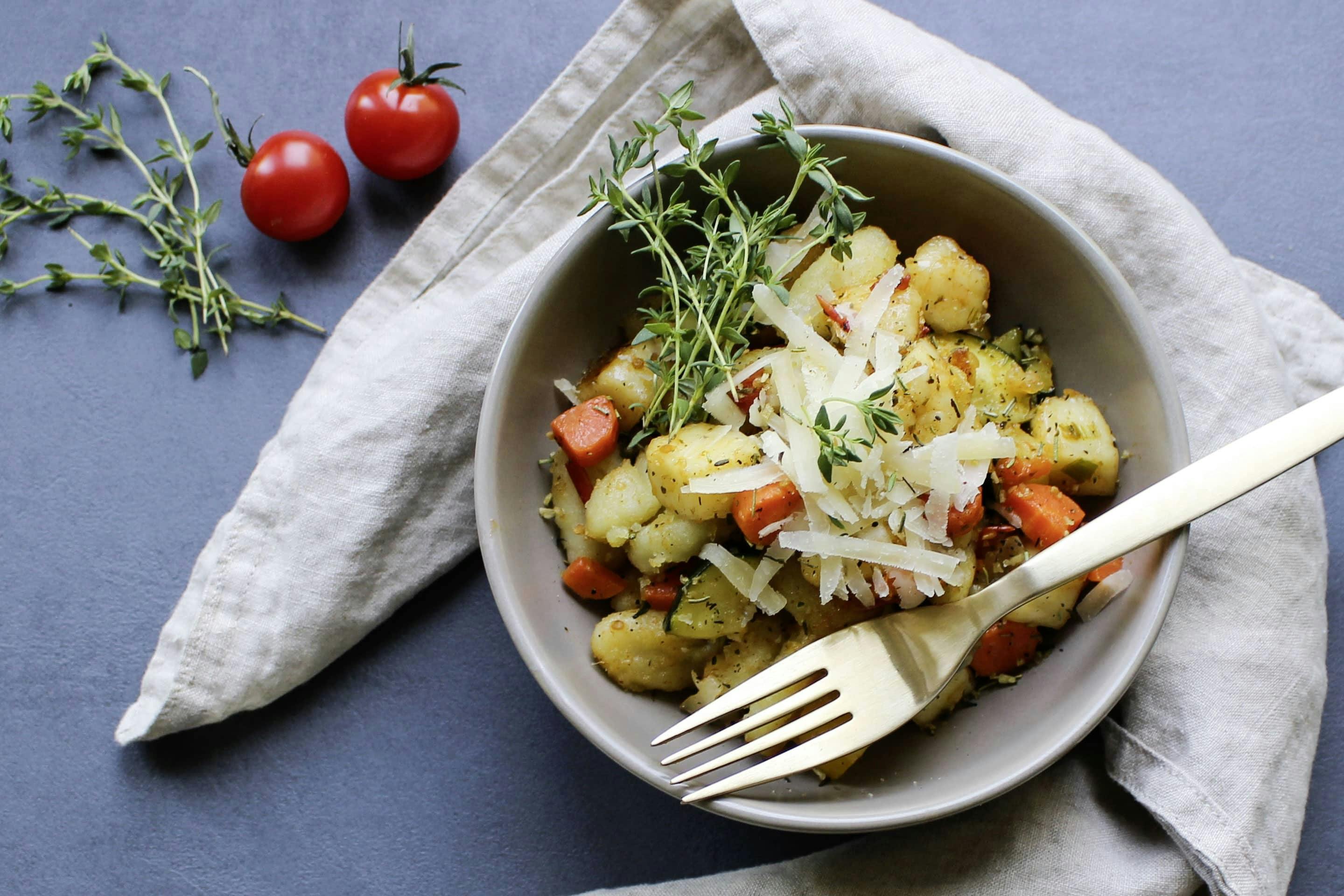 Gnocchi with grilled vegetables and halloumi in a light gray bowl with a golden fork, parmesan and fresh thyme sprigs