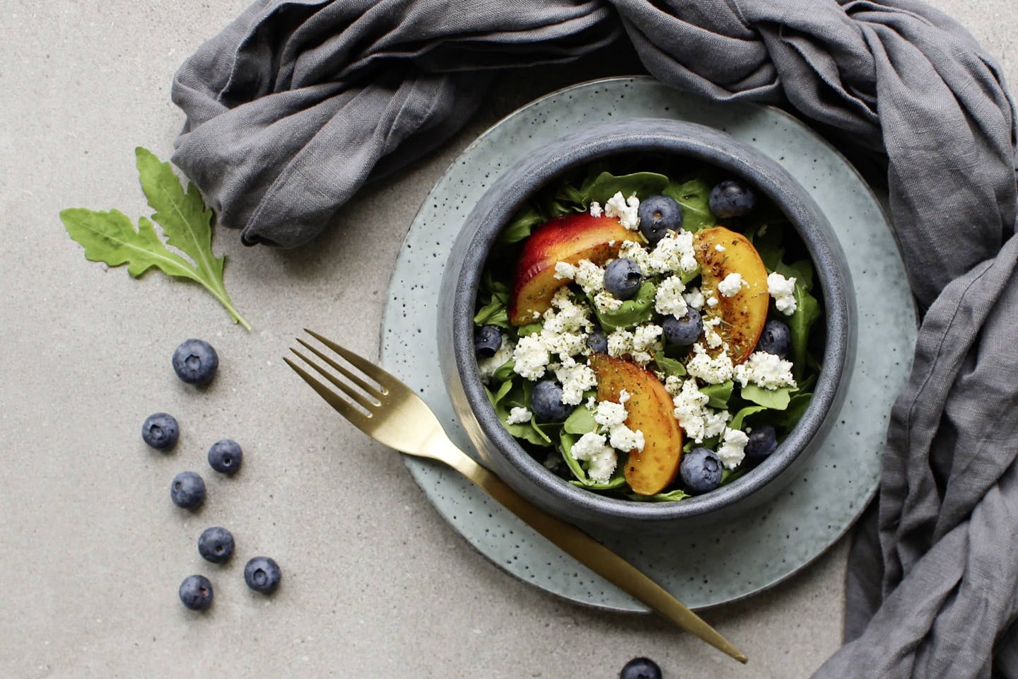 Salad with crumbled goat cheese, fresh blueberries and peach in a light blue bowl