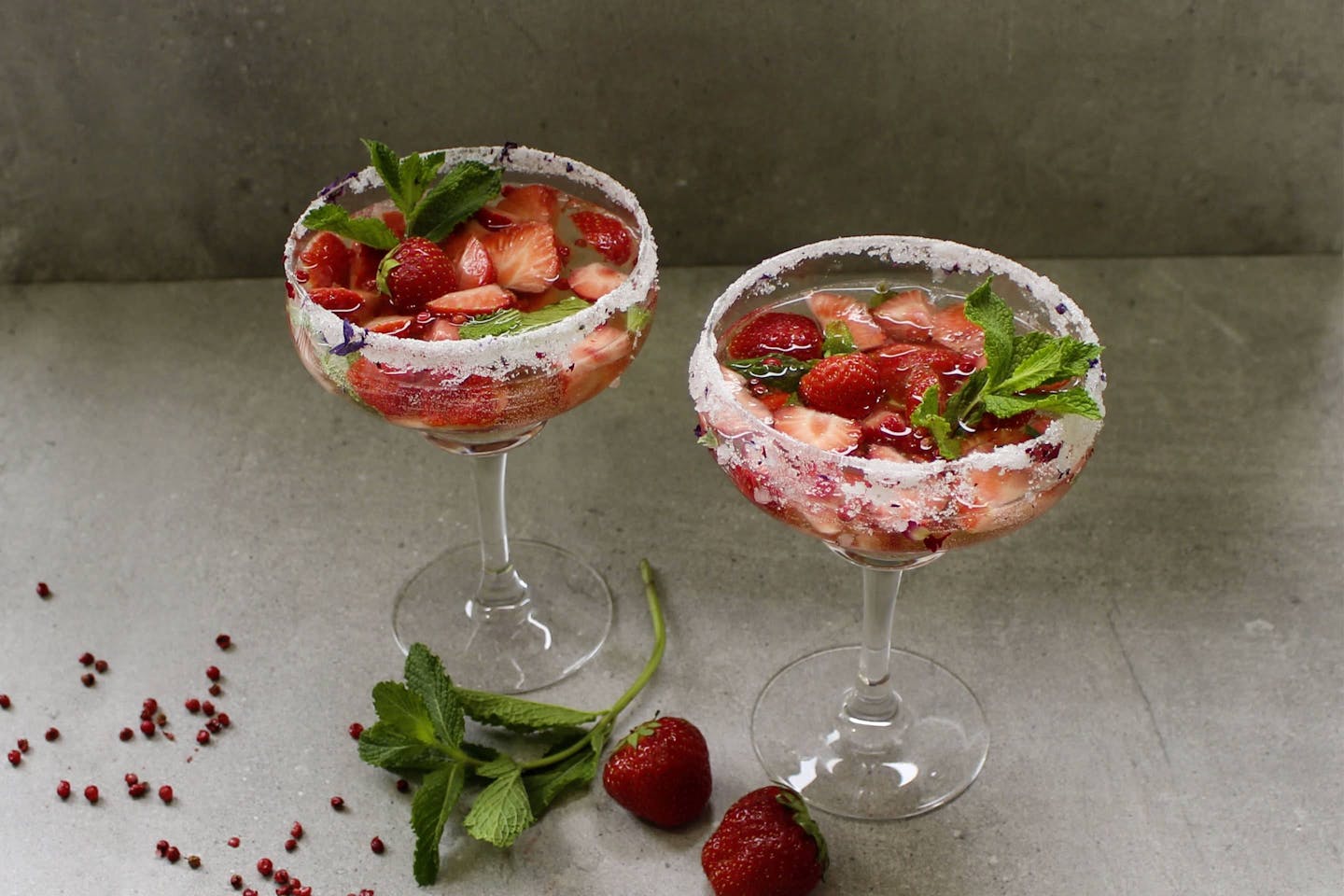 Summer punch with pink berries and fresh strawberry pieces in sugar-coated cocktail glasses, garnished with fresh mint