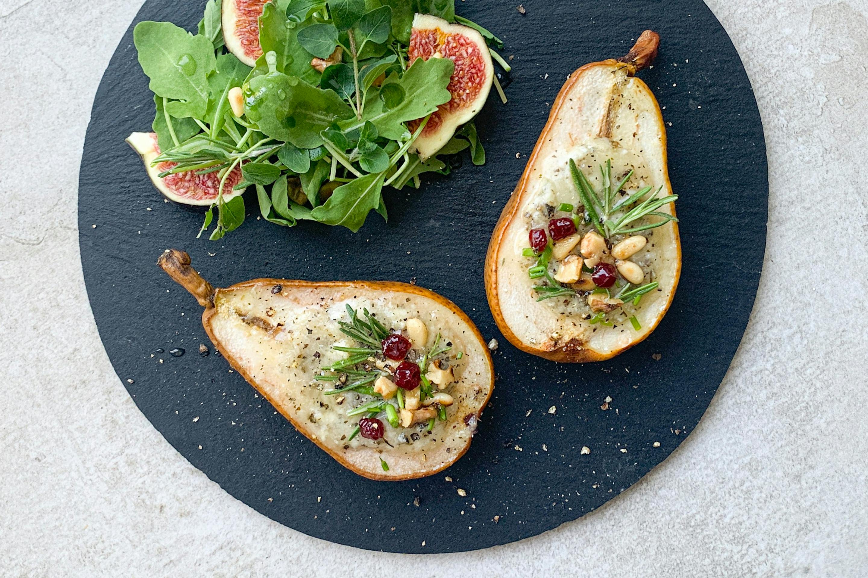 filled half pears along with salad and figs on a black plate