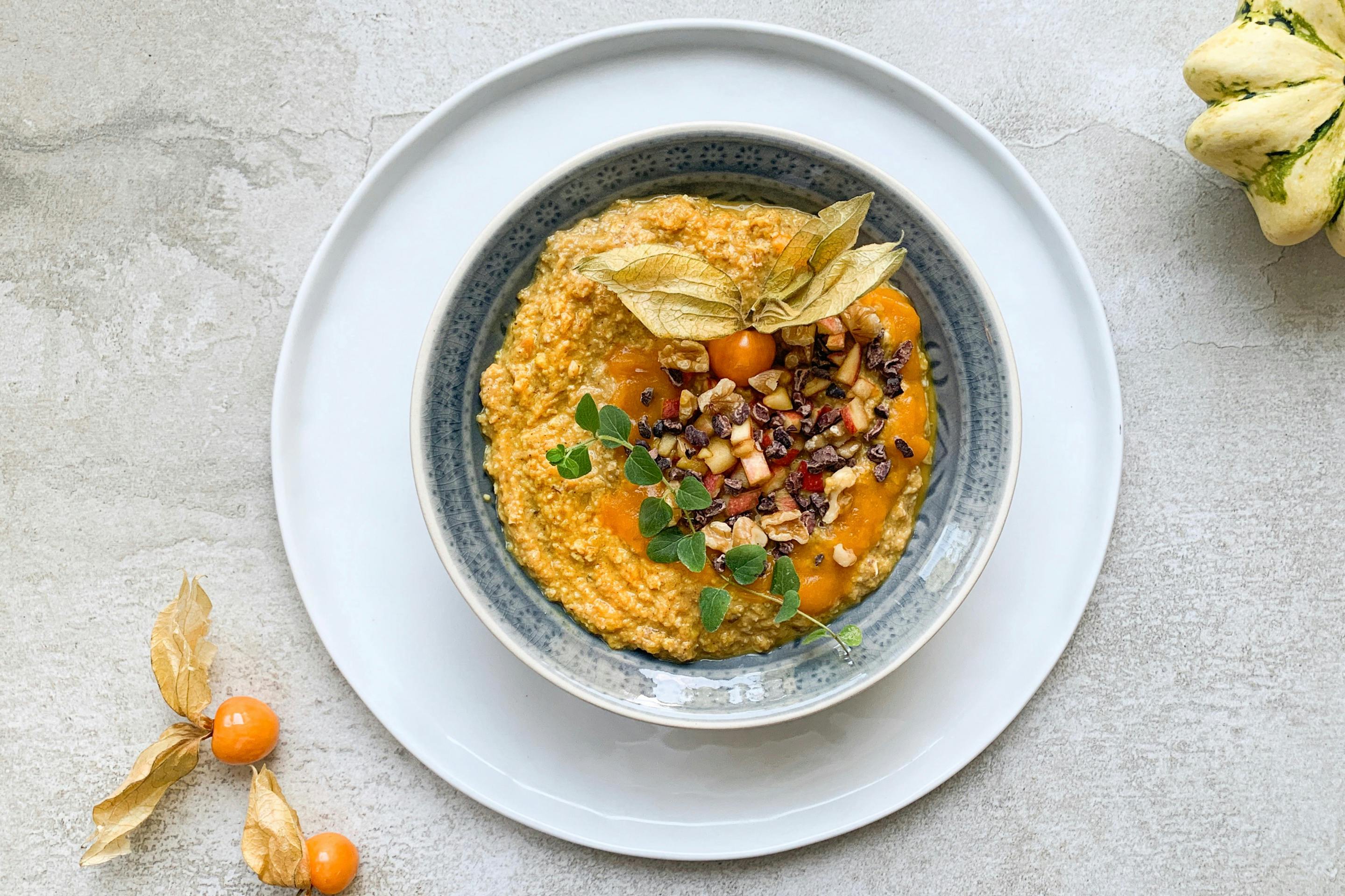 golden pumpkin porridge placed in a lightblue bowl and topped with apple pieces and nuts