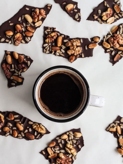 a cup of coffee in the middle of chocolate pieces on a white surface