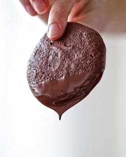 two fingers holding a chocolate cookie with dripping chocolate