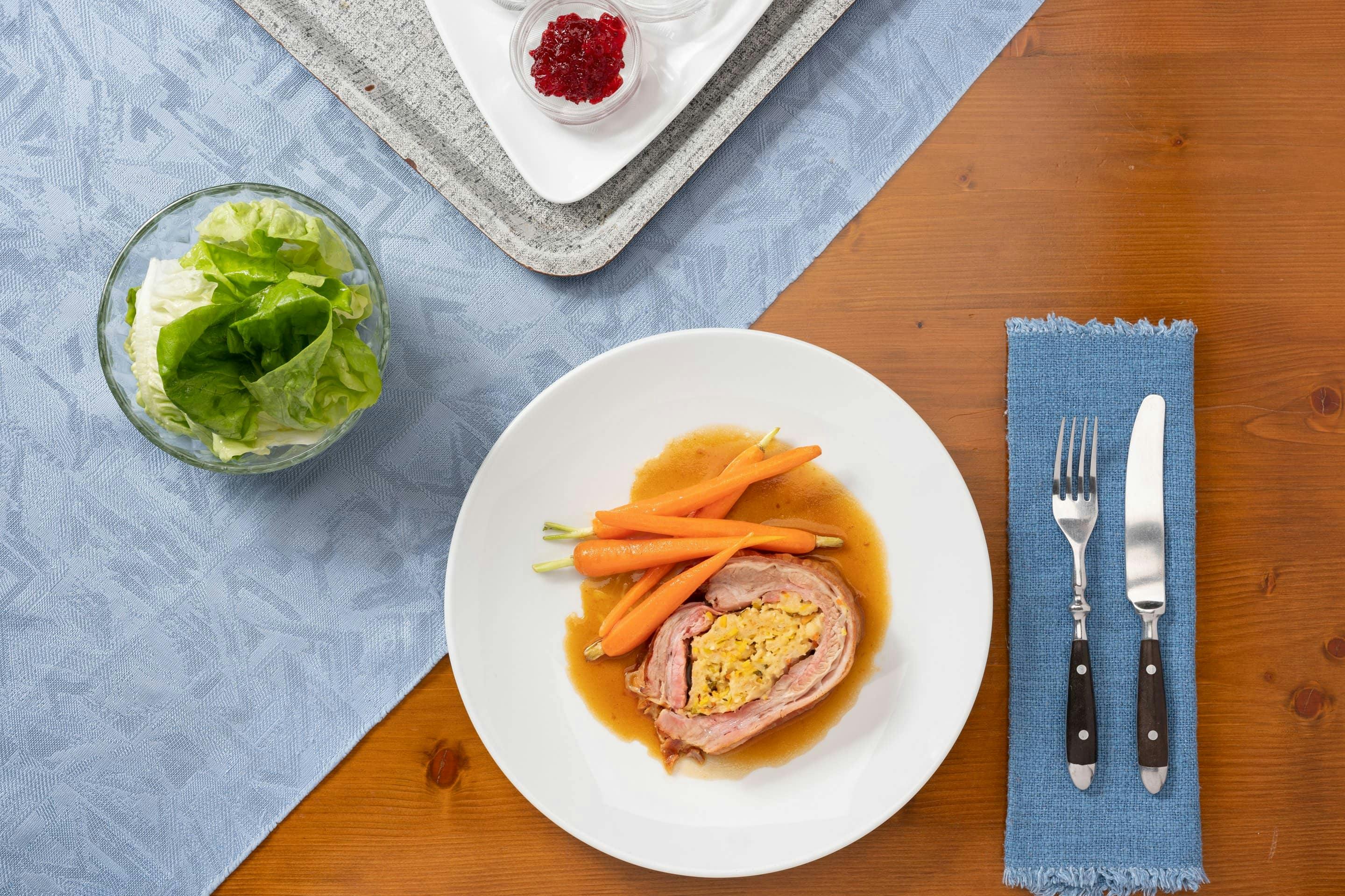 Two pieces of stuffed veal breast with glazed carrots on a white plate.