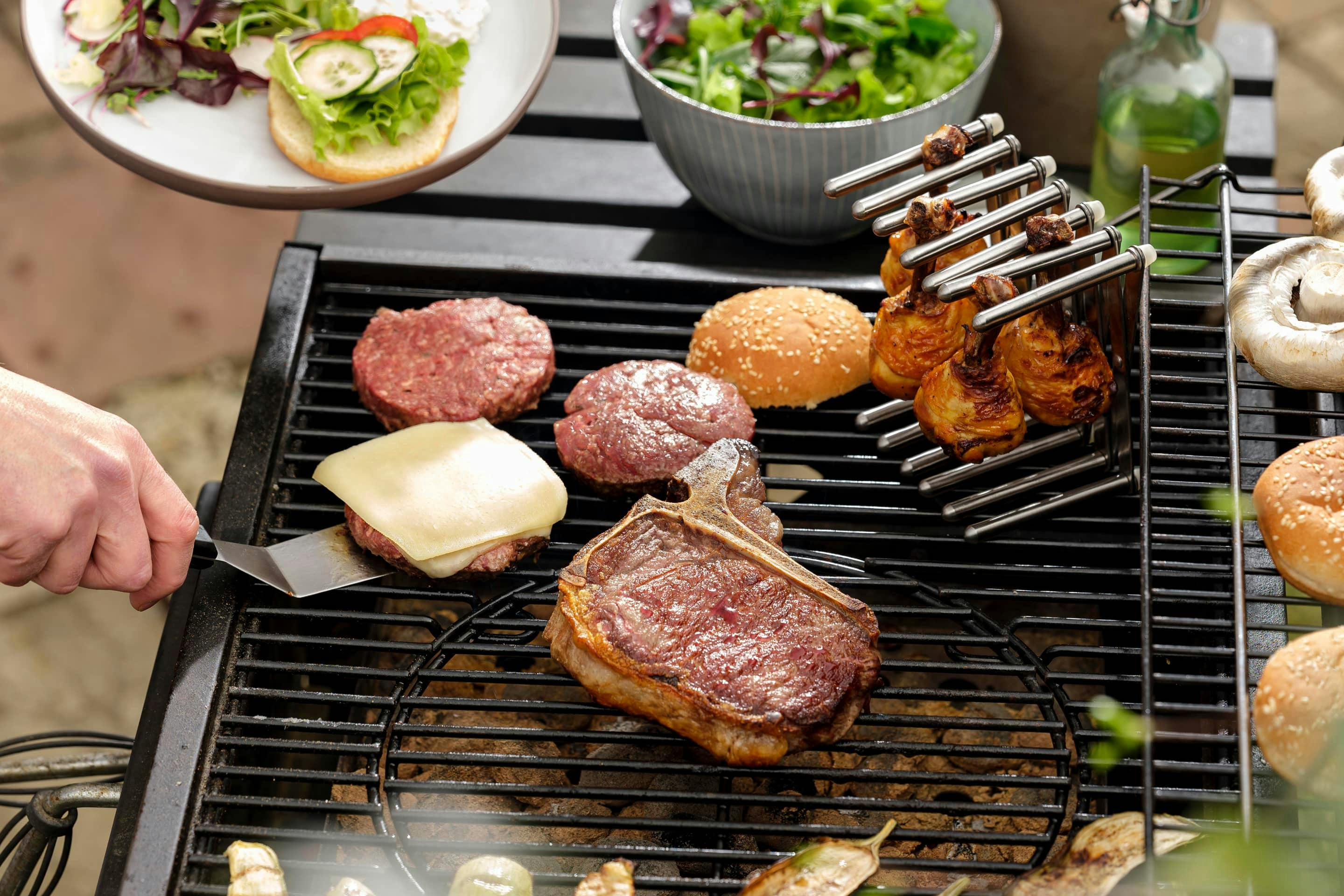 Burger patties, chicken drumsticks and steak on a grill.