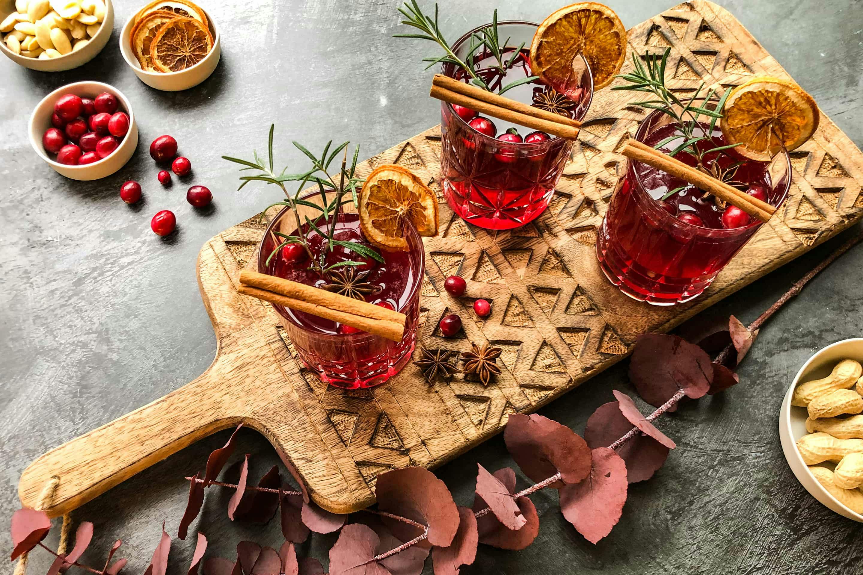 Cranberry spice mimosas on a wooden board with cinnamon, rosemary and orange slices.