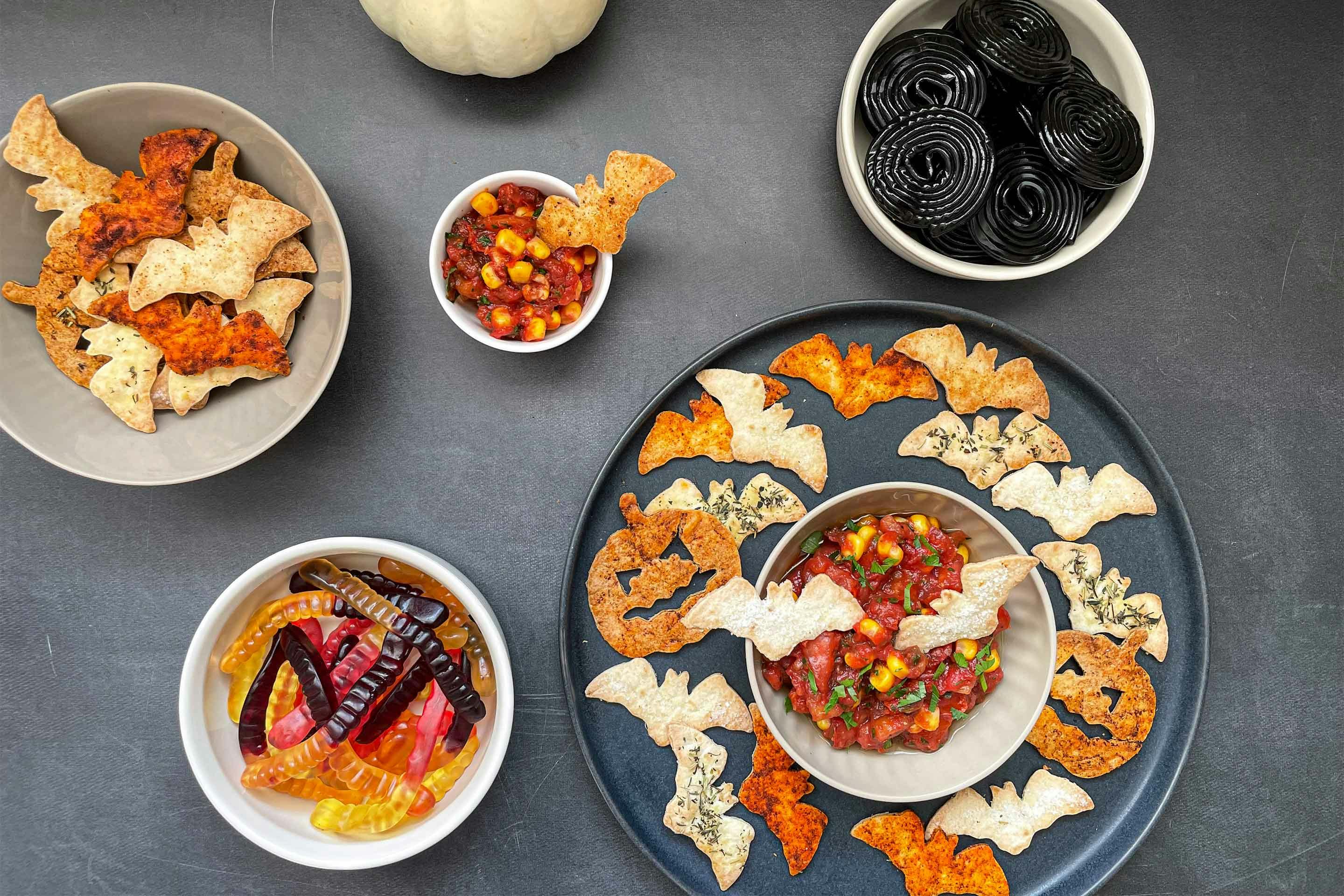 Spicy Halloween chips with red tomato dip and two bowls of candy.