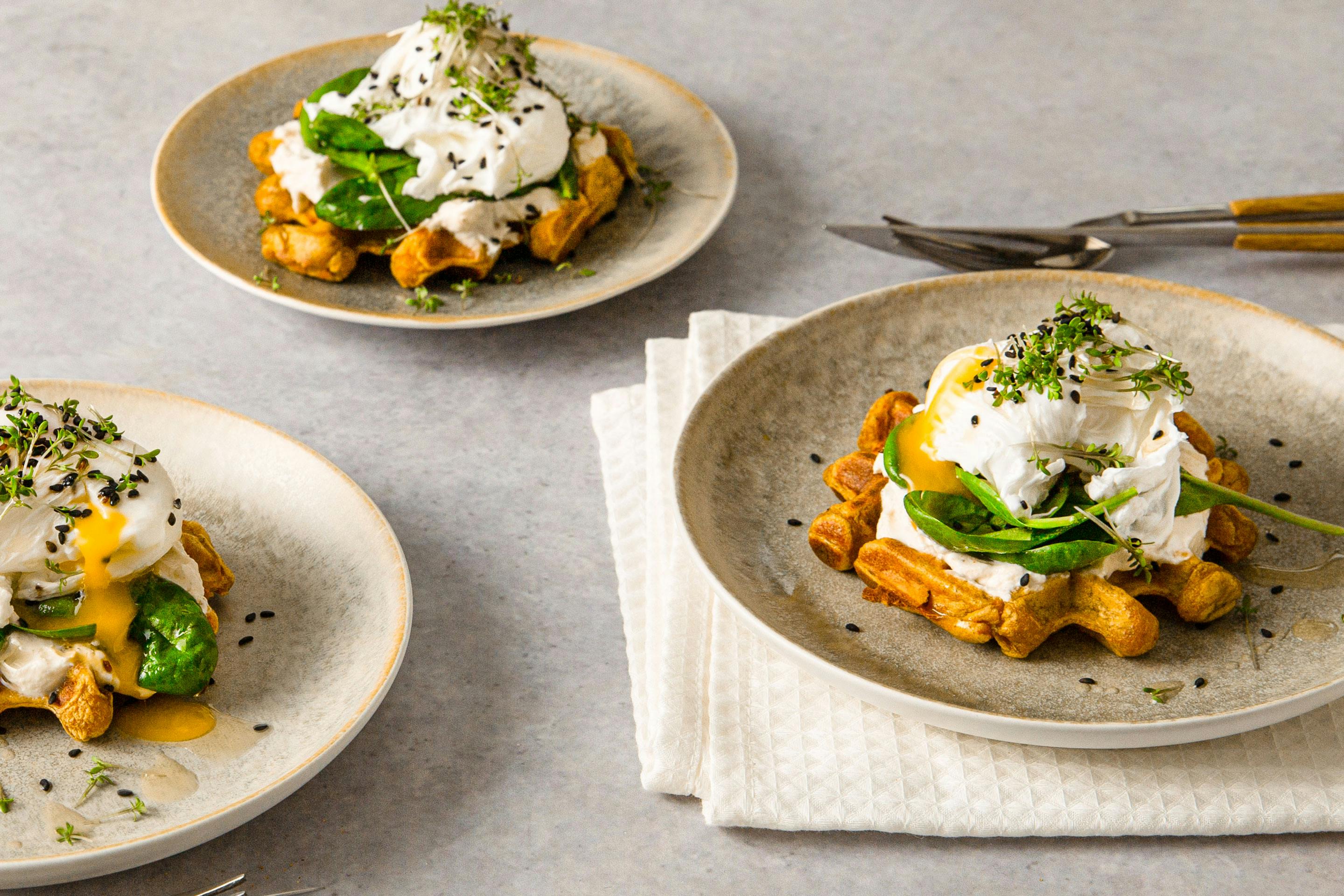 Sweet potato waffle with quark and poached egg stacked on 3 plates and sprinkled with herbs