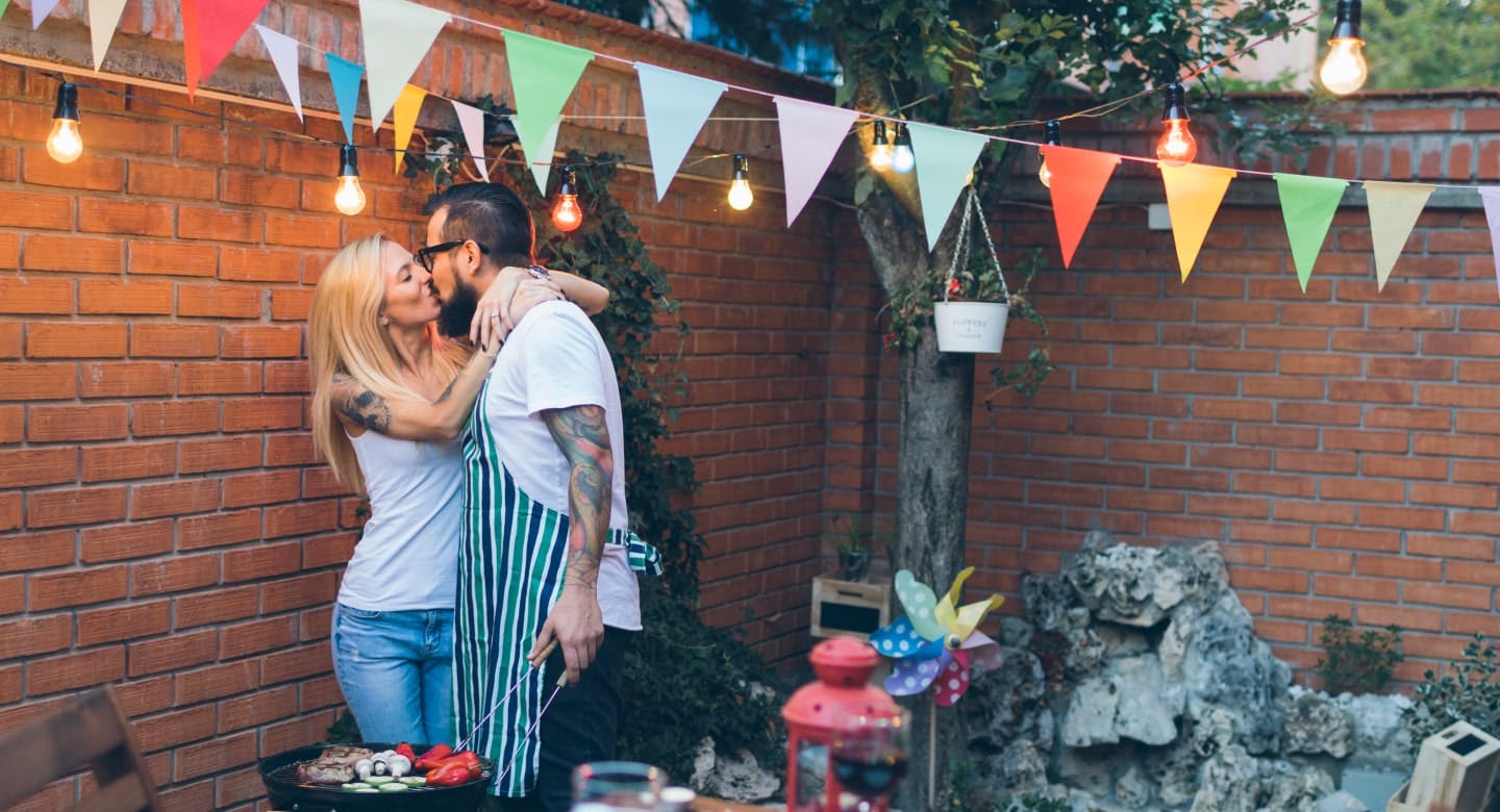 A couple kissing while food is on the grill.